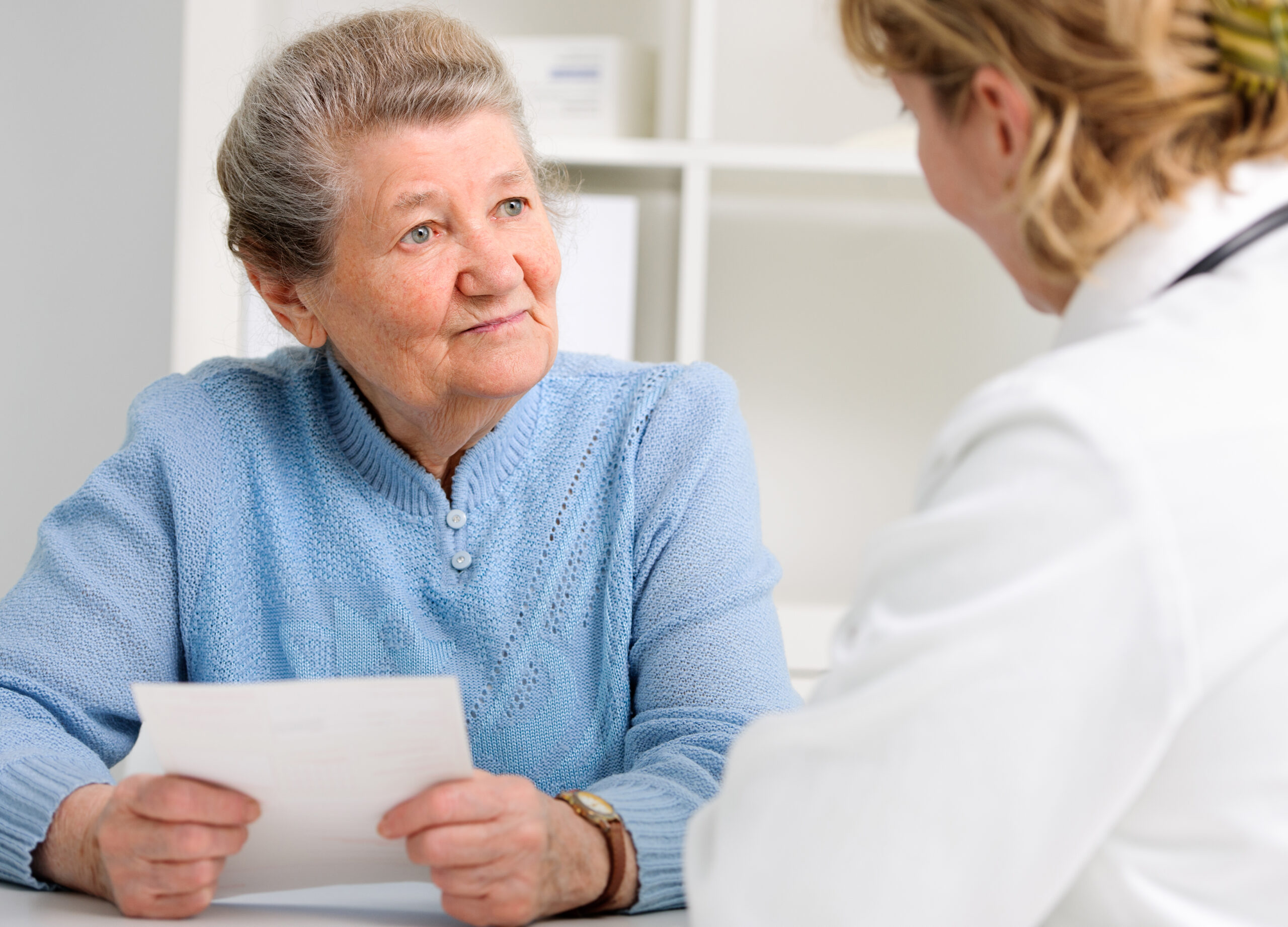 An older woman holding a document talks with a clinician during a medical visit